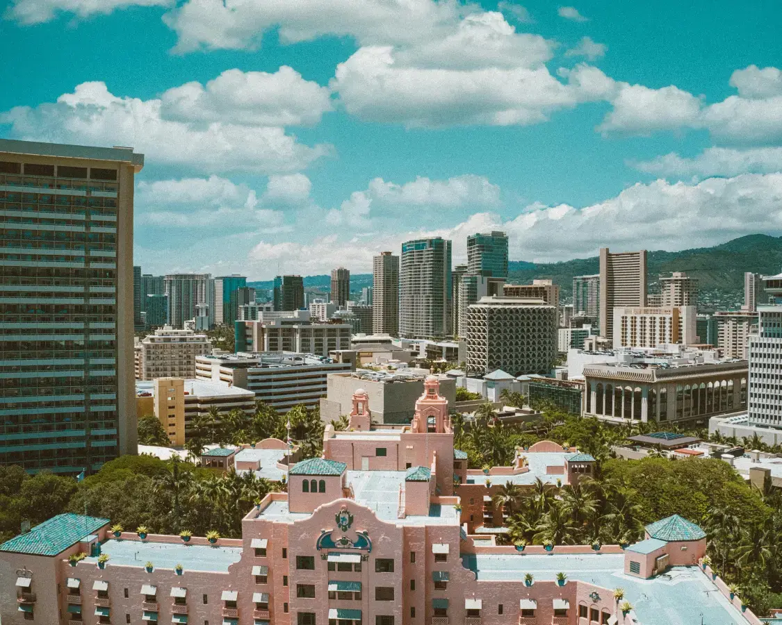An aerial view of a vibrant cityscape featuring a historic-looking pink building in the foreground, with many modern high-rise residential buildings and mountains in the background. The image represents the diverse and evolving urban real estate markets where sale-leaseback solutions are a relevant option.