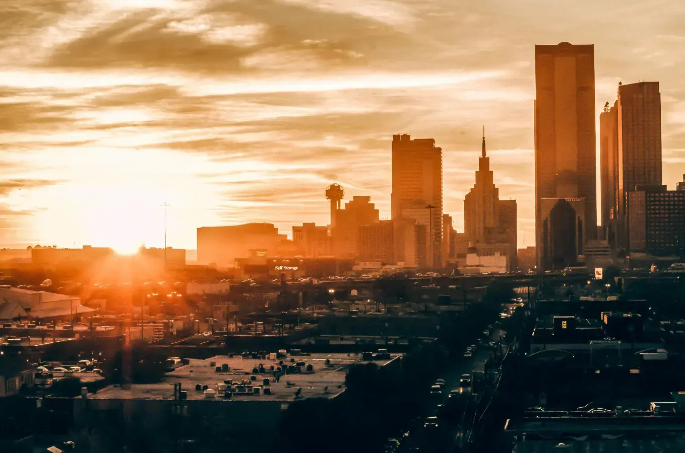 A cityscape is bathed in a warm, golden light as the sun sets behind a skyline of tall modern buildings. The image represents the vibrant opportunities and growth within a major urban real estate market, where a sale-leaseback can be a valuable tool for homeowners.
