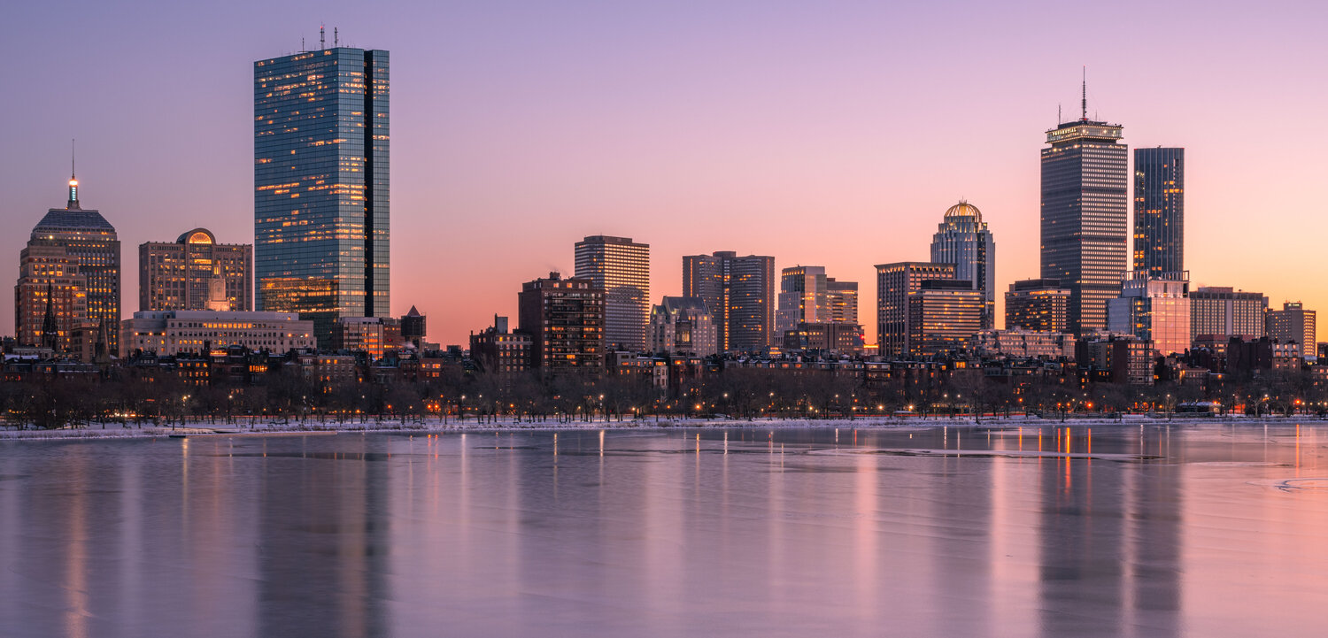 The Boston city skyline at sunset, with the frozen Charles River in the foreground.