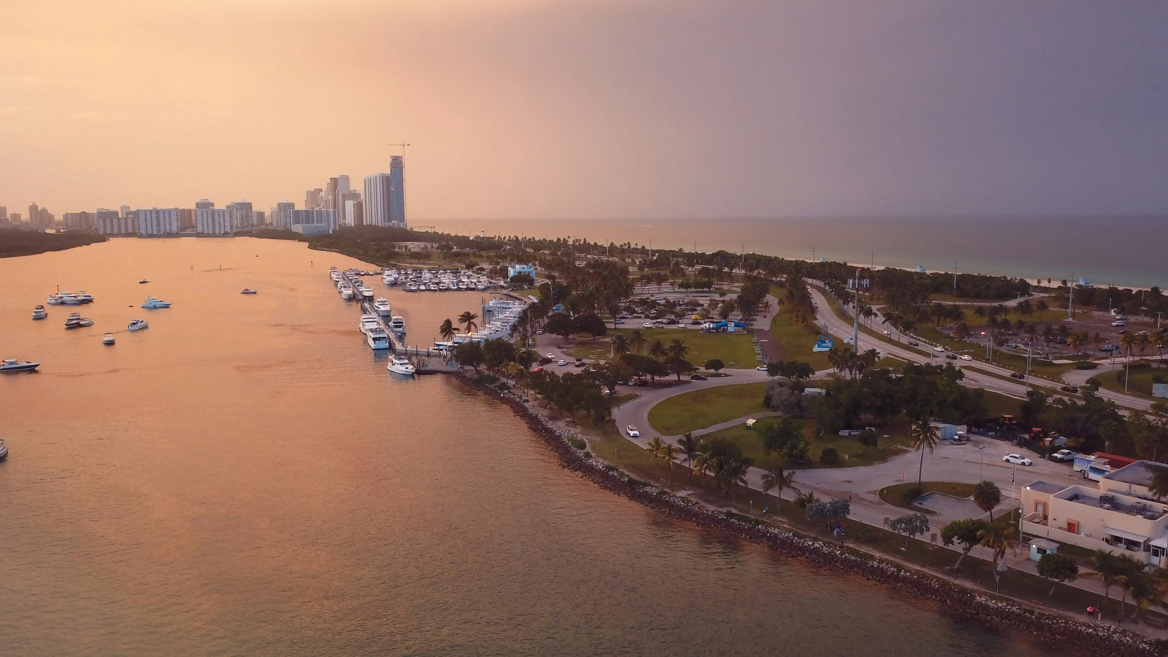 An aerial view of the Miami, Florida coastline at sunset, with a marina full of boats and a cityscape in the background.