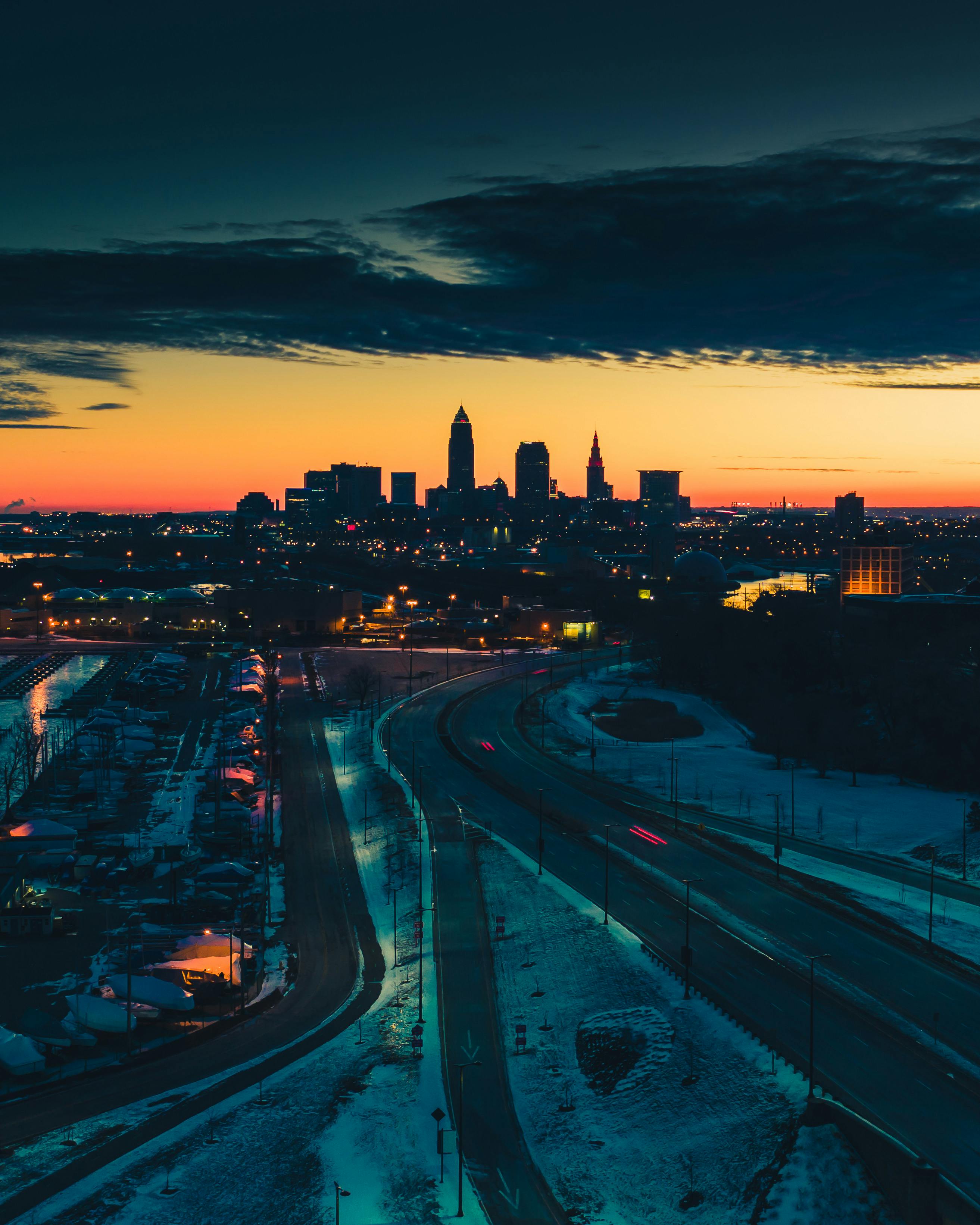 The Cleveland, Ohio skyline at sunrise, with a snow-covered highway in the foreground and a bright orange sky.