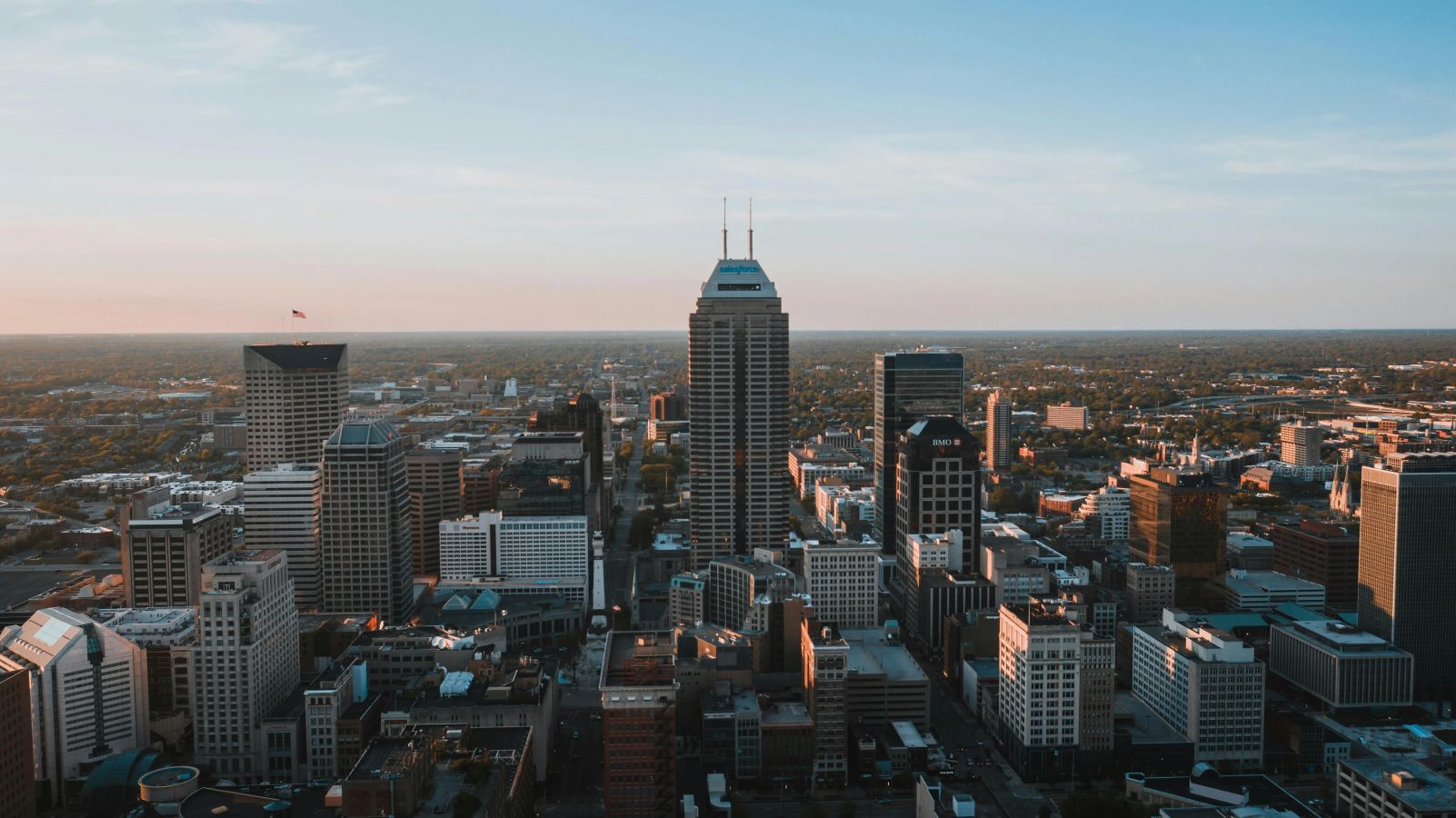 An aerial view of a city skyline at sunset, showing a dense collection of modern and older buildings and a suburban area stretching into the distance. The image represents a large, dynamic metropolitan real estate market where a sale-leaseback is a modern solution for homeowners.